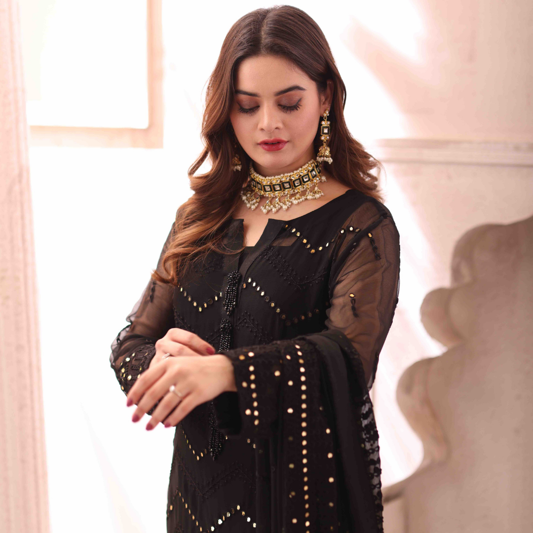 A girl is standing in black 3 Piece Unstiched Embroidered Chiffon Suit looking on her forearm.