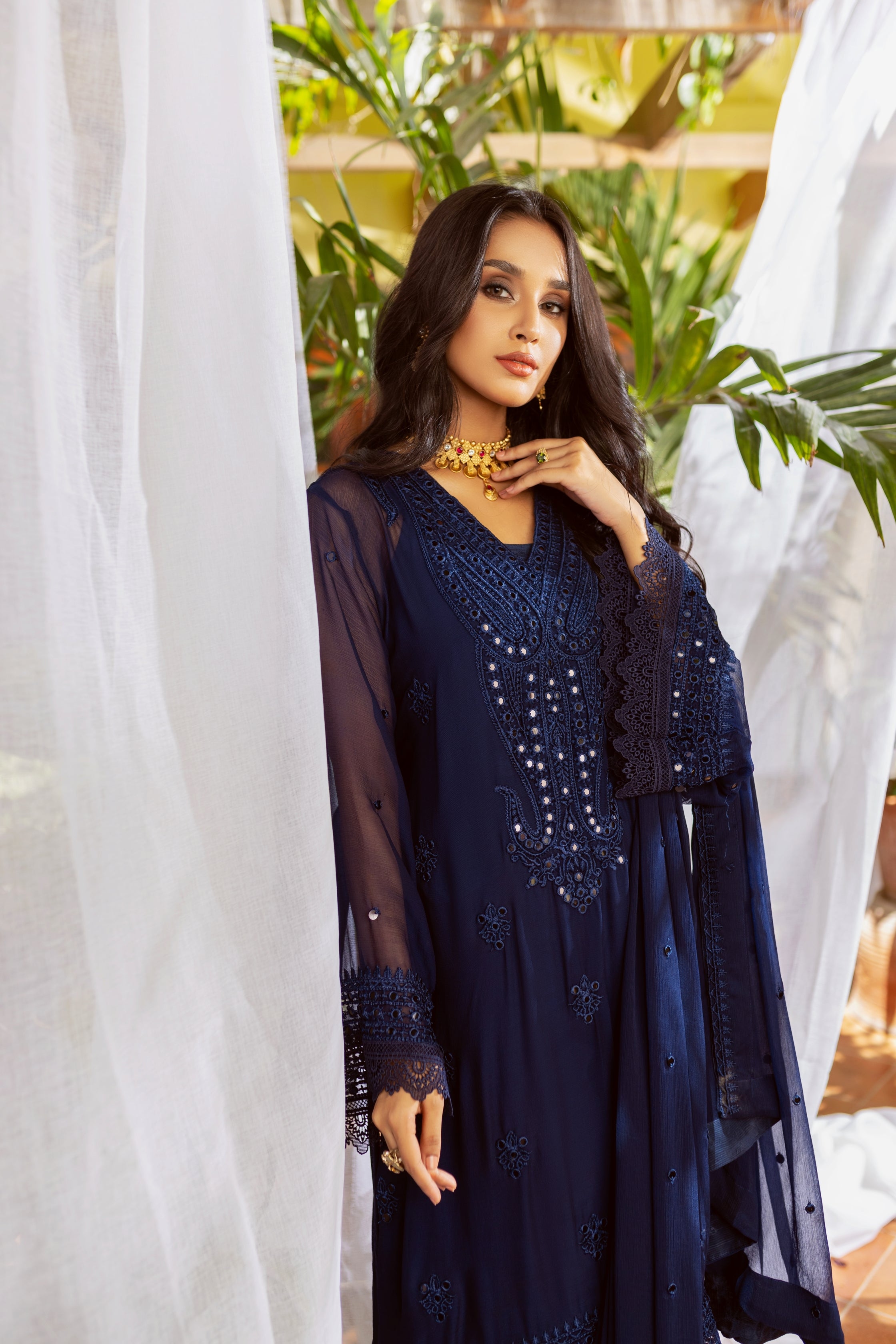 A girl in Blue chiffon suit standing in front of plants.