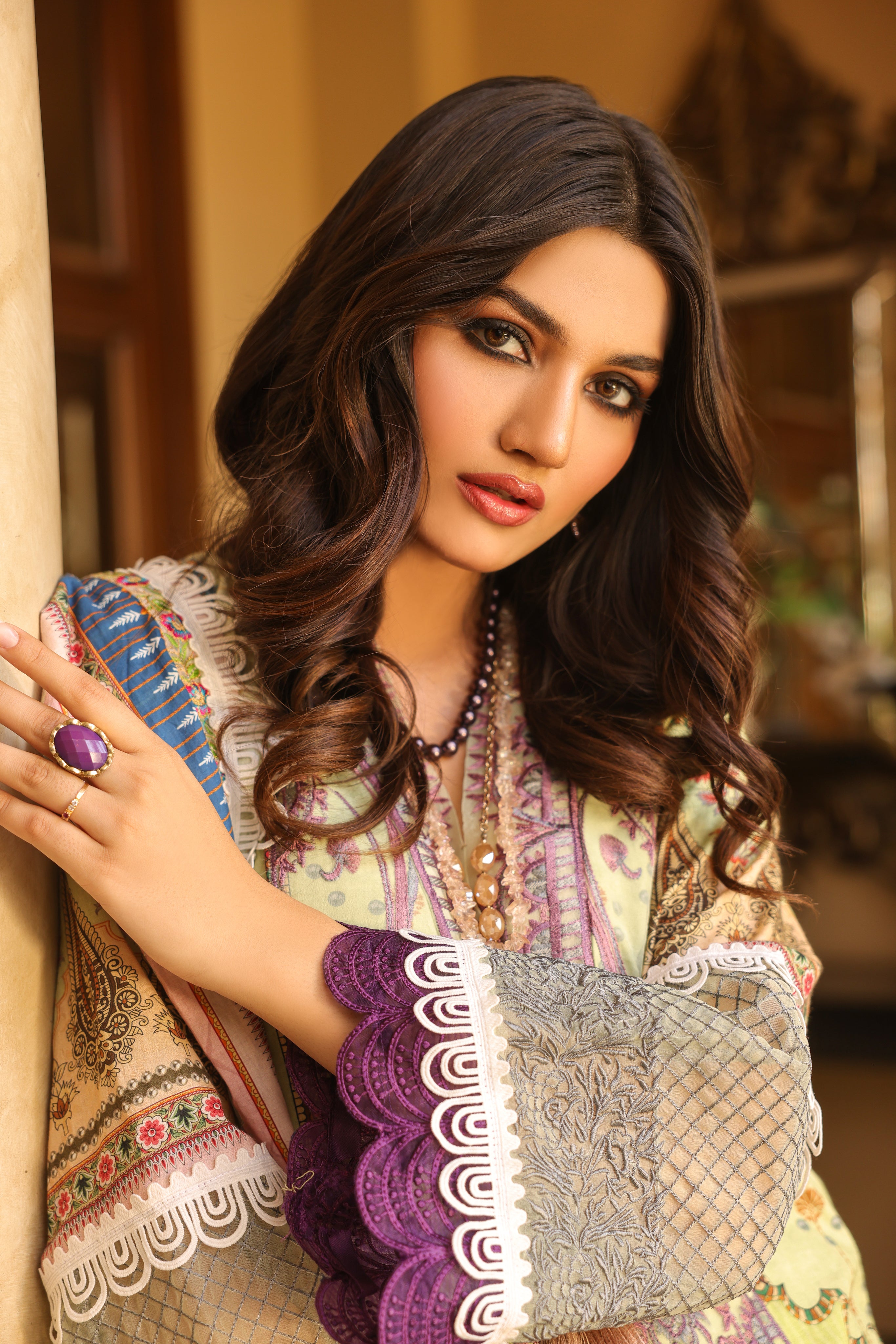 A girl is leaning to an object with a violt purple ring in her hand while wearingDigital Lawn Suit with Embroidered Selves.